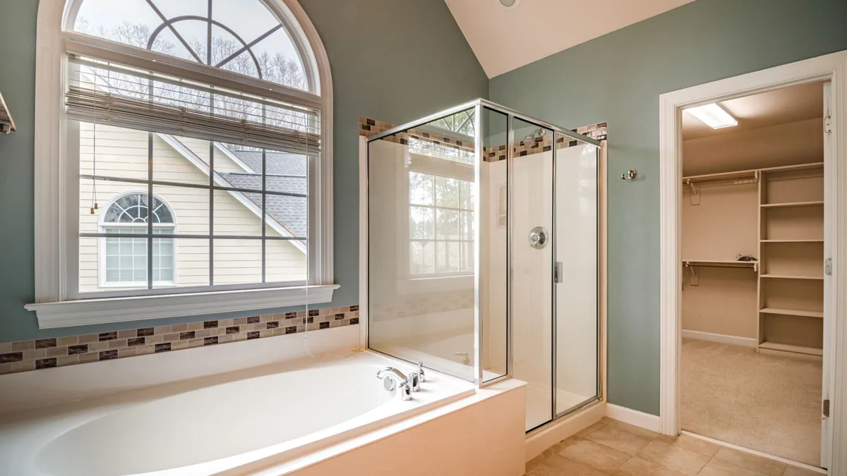 Wide bright master bath: white garden tub, glass shower, arched window, walk-in closet door