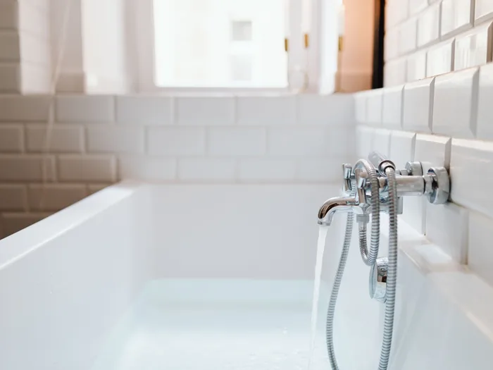 Close detail of a white tub filling from a chrome wall faucet, subway tile