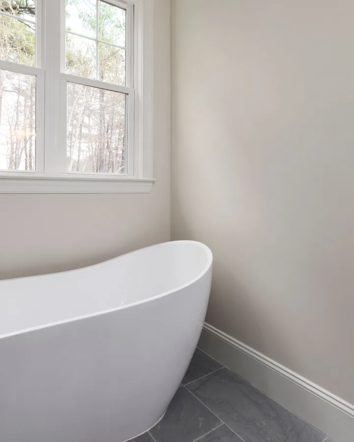White freestanding slipper tub under a window, gray tile floor