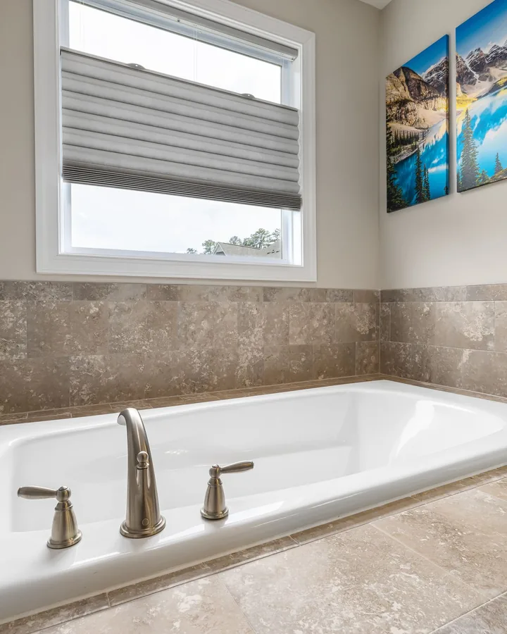 White drop-in tub in a stone-look tile deck, canvas landscape prints on wall