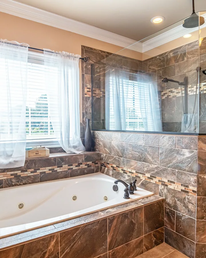 White jetted tub in brown stone tile beside a glass tile shower