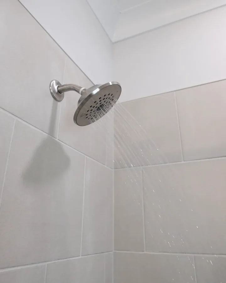 Chrome shower head spraying across large light tile shower walls