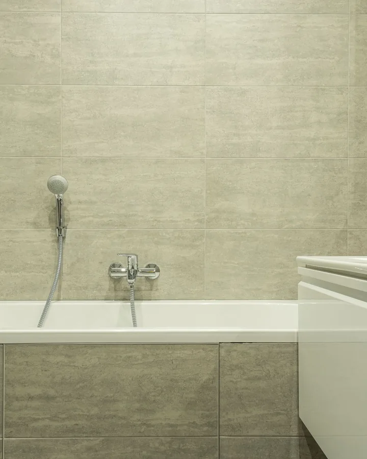 White built-in tub with gray tile front and walls, hand shower, vanity edge