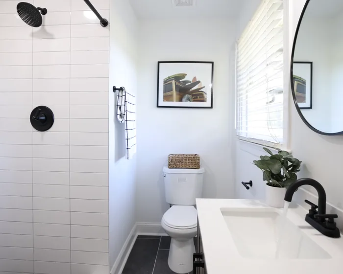 Bright small bathroom: white subway tile shower, toilet, white vanity, round mirror