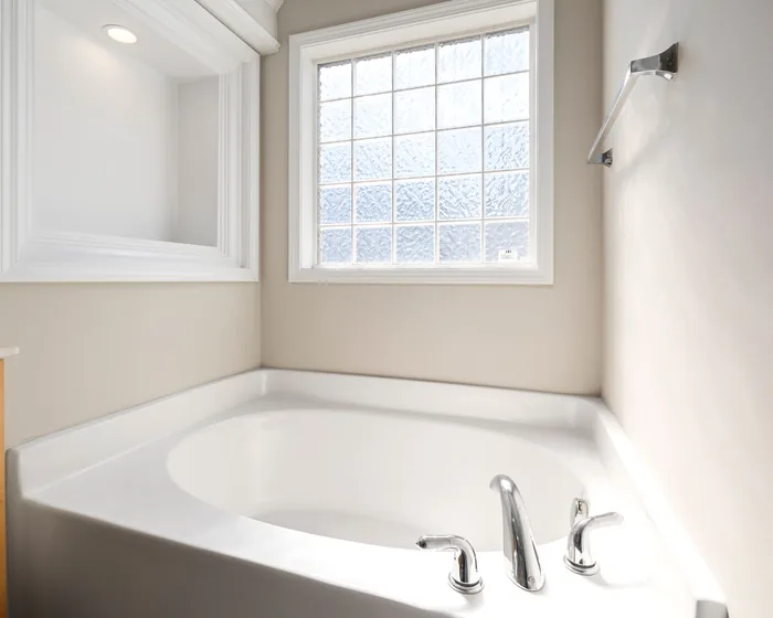 Clean white corner tub with chrome faucet under a glass-block window