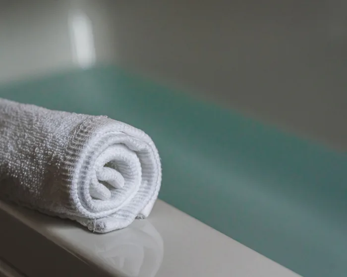 Close detail of a tub rim with a rolled white towel, shallow focus