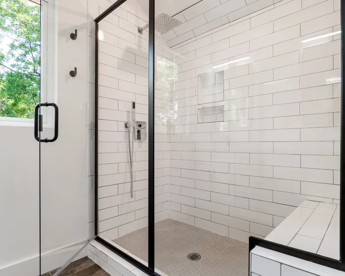 White subway tile walk-in shower, black-frame glass door, tile bench